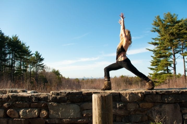 A young woman practices yoga on a wall in a clearing in a pine forest.