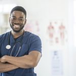 Male nurse standing in scrubs smiling.