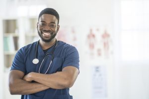 Male nurse standing in scrubs smiling.