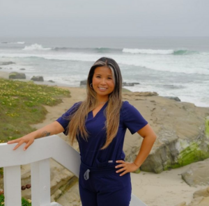 A photo of May Tran in scrubs standing in front of the ocean.
