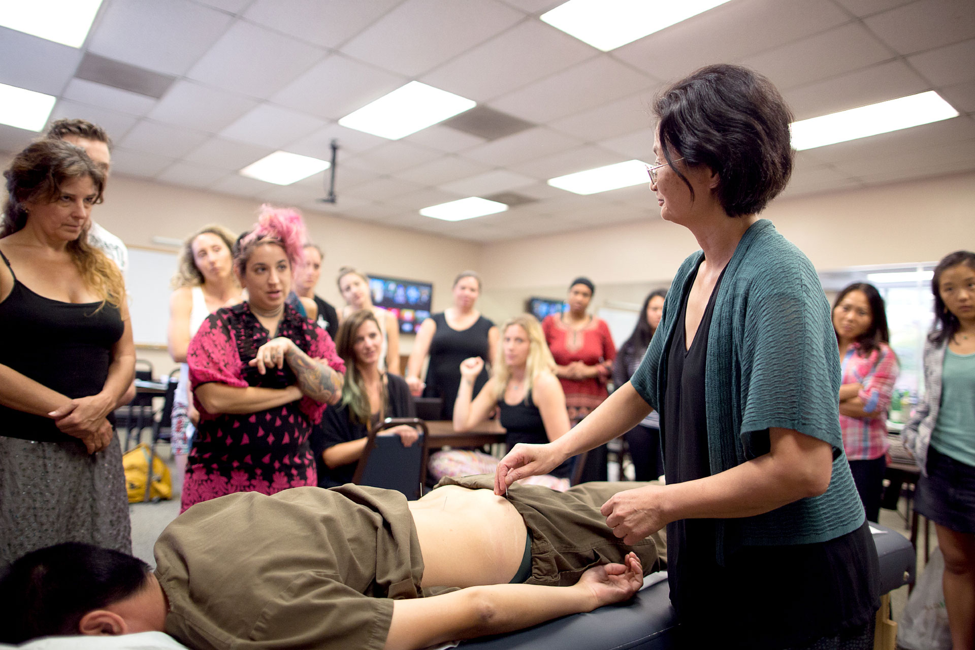 Experienced acupuncture instructor demonstrating technique to students in a classroom setting