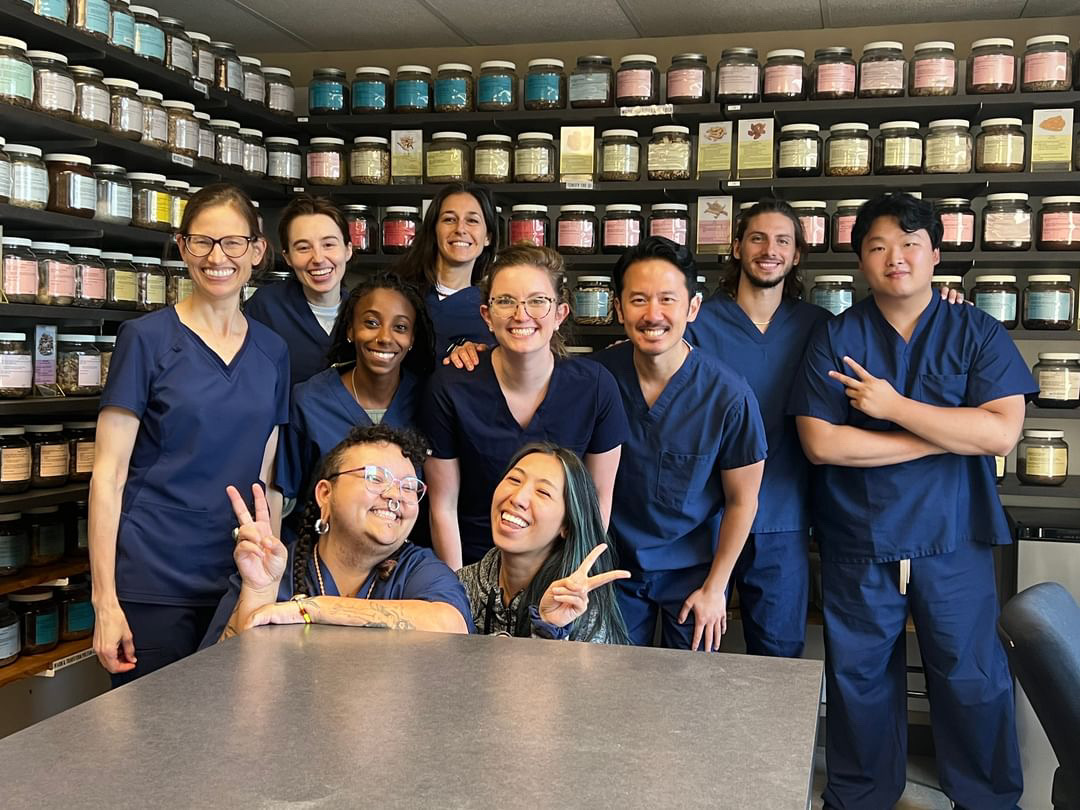 Acupuncture students and instructors in scrubs pose together in a Chinese herbal medicine dispensary