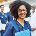 Nurse holding a clipboard with a healthcare team behind her in a clinical setting