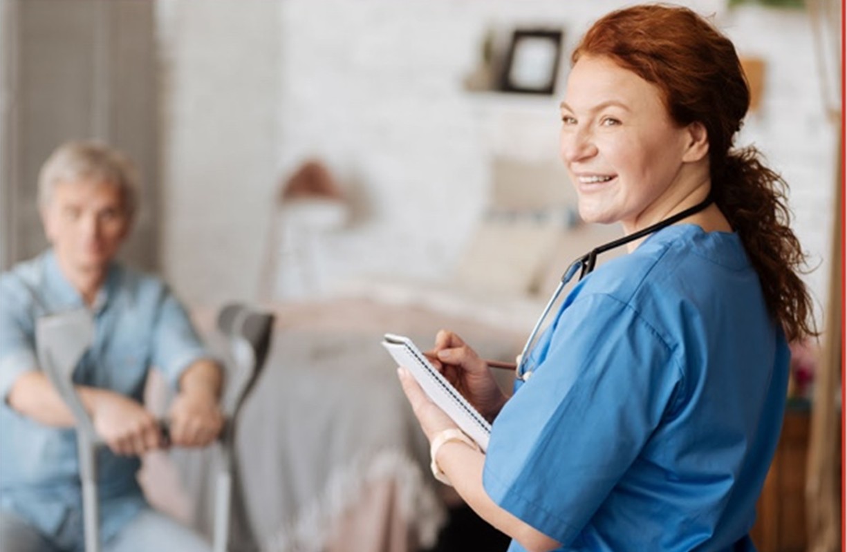 Nurse in scrubs taking notes while caring for a patient in a home healthcare setting
